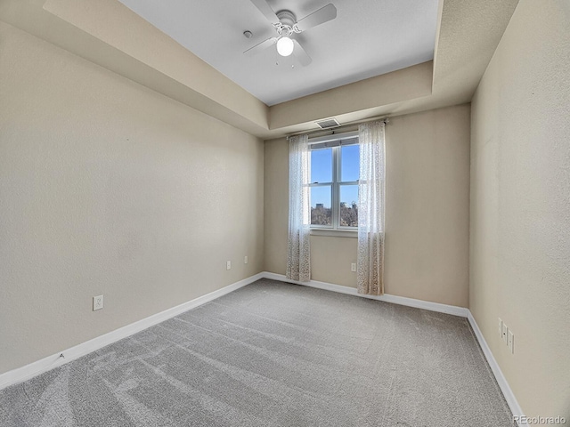 carpeted empty room with a raised ceiling and ceiling fan