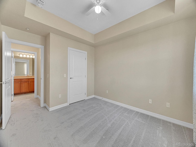 unfurnished bedroom with light colored carpet, ceiling fan, and a tray ceiling