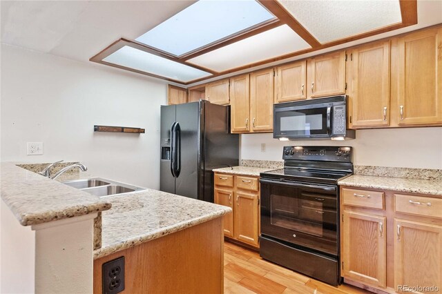 kitchen featuring a skylight, light stone countertops, sink, light hardwood / wood-style flooring, and black appliances