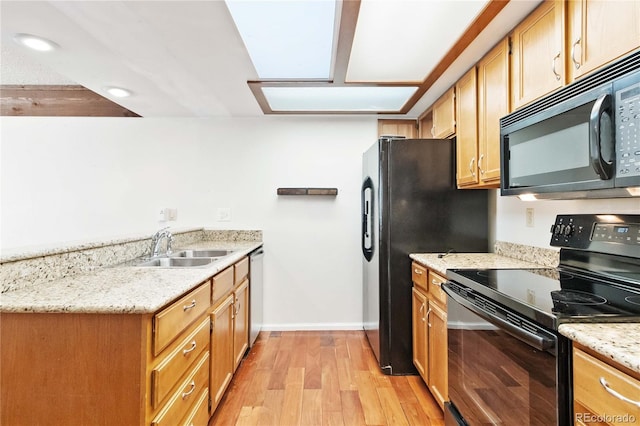 kitchen featuring a skylight, sink, light stone counters, light hardwood / wood-style flooring, and black appliances