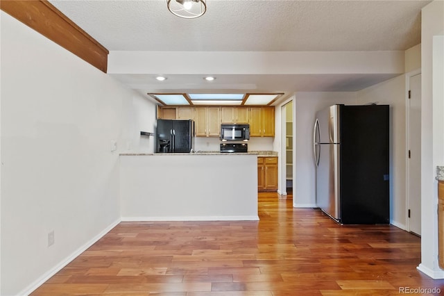 kitchen with a textured ceiling, light wood-type flooring, light stone counters, and black appliances