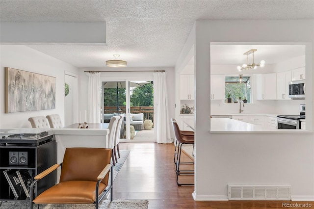8369 W 77th Way, Arvada, CO 80005 - kitchen with appliances with stainless steel finishes, a textured ceiling, healthy amount of natural light, white cabinets, and a kitchen bar