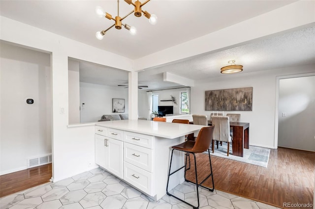 8369 W 77th Way, Arvada, CO 80005 - kitchen featuring a chandelier, light countertops, a peninsula, white cabinets, and a kitchen bar