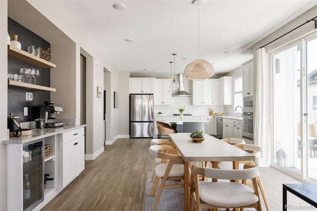 kitchen with wall chimney exhaust hood, a healthy amount of sunlight, pendant lighting, stainless steel appliances, and white cabinetry