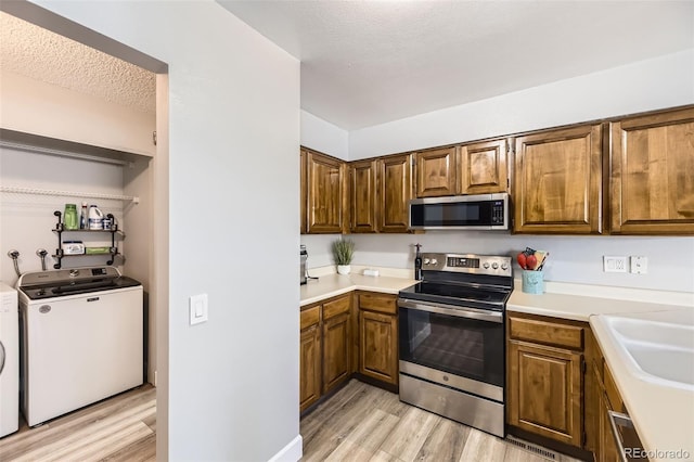 10685 W Apishapa Pass, Littleton, CO 80127 - kitchen with appliances with stainless steel finishes, light wood finished floors, light countertops, brown cabinets, and independent washer and dryer