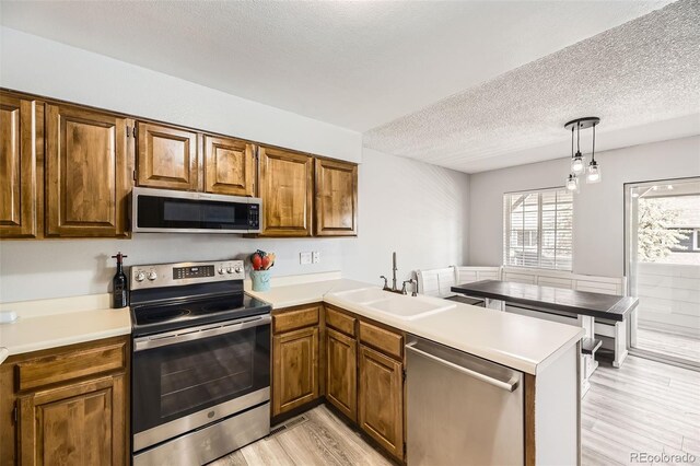 10685 W Apishapa Pass, Littleton, CO 80127 - kitchen featuring appliances with stainless steel finishes, a sink, a peninsula, light wood-style flooring, and a textured ceiling