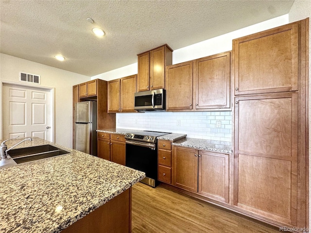 3865 Presidio Pt Unit 101, Colorado Springs, CO 80920 - kitchen featuring appliances with stainless steel finishes, a sink, a textured ceiling, brown cabinets, and wood finished floors