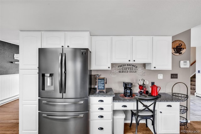 kitchen featuring stainless steel fridge, dark stone counters, baseboard heating, wood-type flooring, and white cabinetry