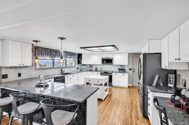 kitchen with sink, hanging light fixtures, light wood-type flooring, appliances with stainless steel finishes, and white cabinetry