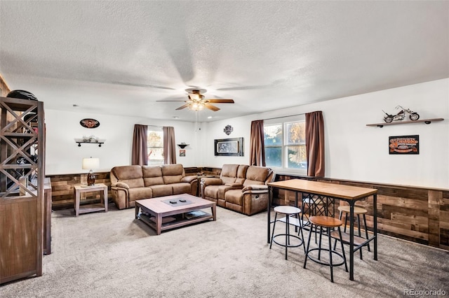 carpeted living room with a textured ceiling, ceiling fan, and wood walls