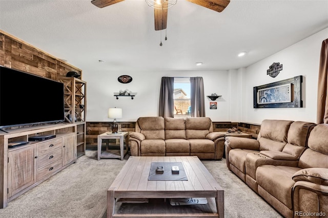 living room featuring ceiling fan, wooden walls, light colored carpet, and a textured ceiling