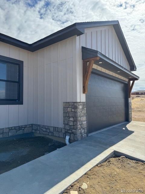 view of side of property featuring a garage, stone siding, board and batten siding, and concrete driveway