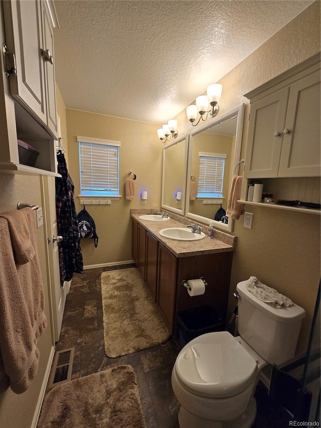 5131 Delphinium Cir, Brighton, CO 80601 - bathroom featuring a textured ceiling, a textured wall, double vanity, toilet, and baseboards