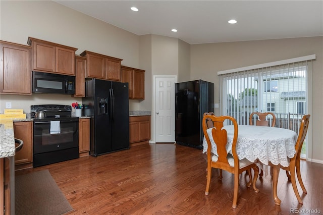 5131 Delphinium Cir, Brighton, CO 80601 - kitchen featuring black appliances, brown cabinets, vaulted ceiling, dark wood finished floors, and light stone counters