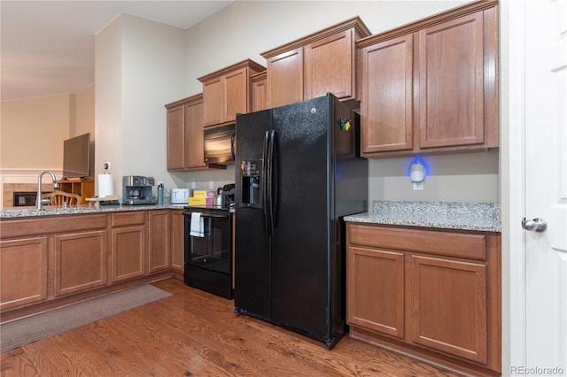 5131 Delphinium Cir, Brighton, CO 80601 - kitchen featuring black appliances, wood finished floors, brown cabinetry, and light stone counters