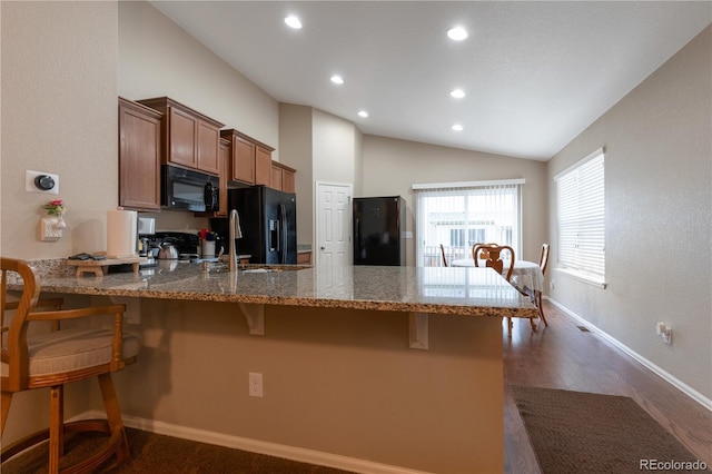 5131 Delphinium Cir, Brighton, CO 80601 - kitchen featuring black appliances, a peninsula, stone countertops, a kitchen bar, and lofted ceiling
