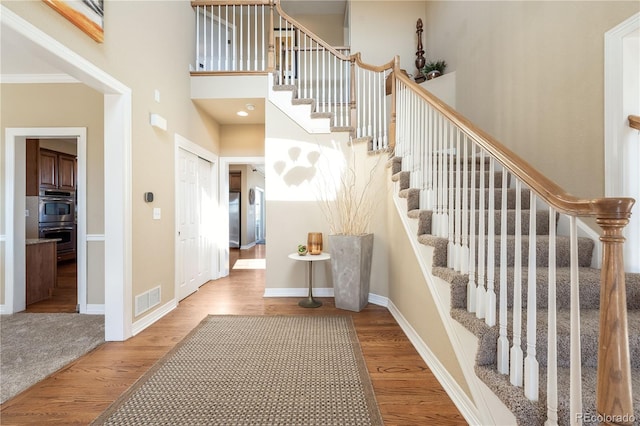 stairs featuring a towering ceiling, wood finished floors, visible vents, and baseboards