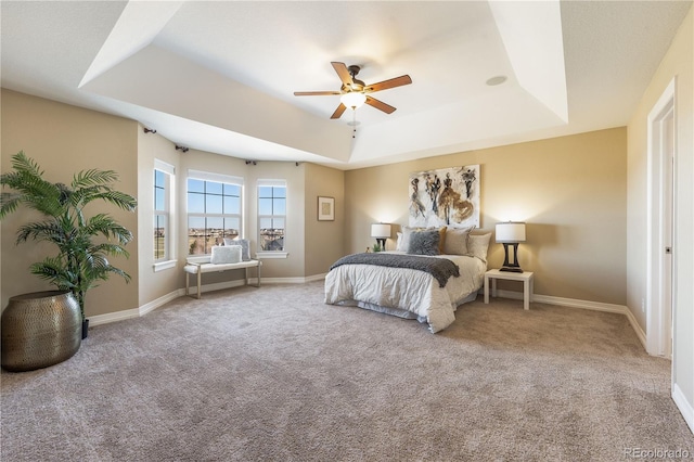 carpeted bedroom with a tray ceiling, a ceiling fan, and baseboards