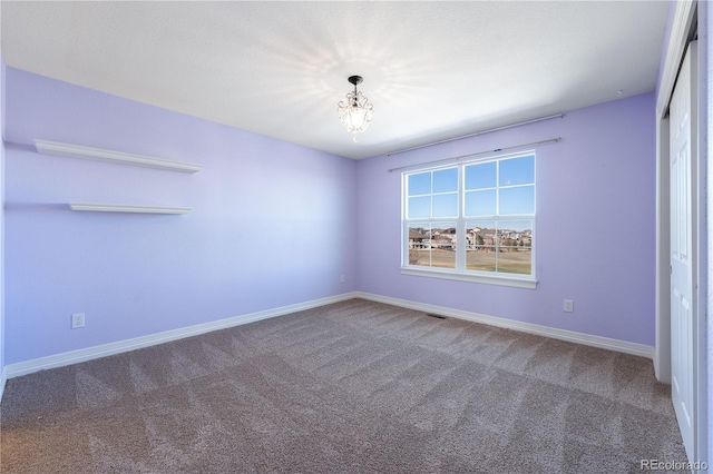 spare room with an inviting chandelier, carpet, visible vents, and baseboards