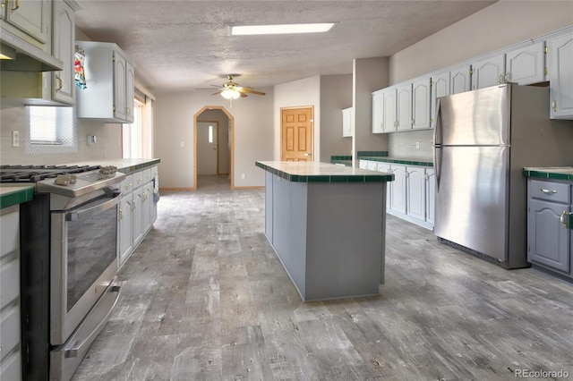 kitchen with hardwood / wood-style floors, tile countertops, white cabinets, ceiling fan, and stainless steel appliances