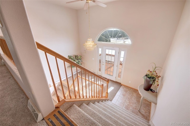 carpeted foyer featuring a high ceiling and ceiling fan with notable chandelier