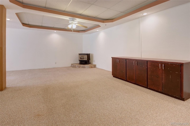 basement with light carpet, a wood stove, and ceiling fan