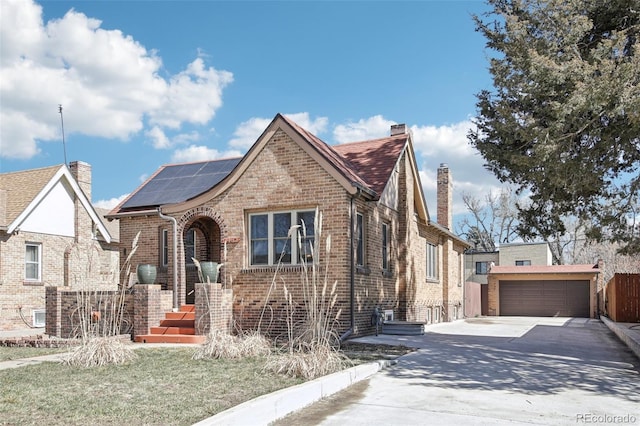 tudor house with an outbuilding, a chimney, a garage, brick siding, and roof mounted solar panels