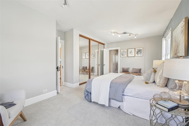 bedroom featuring baseboards, light carpet, a closet, and track lighting