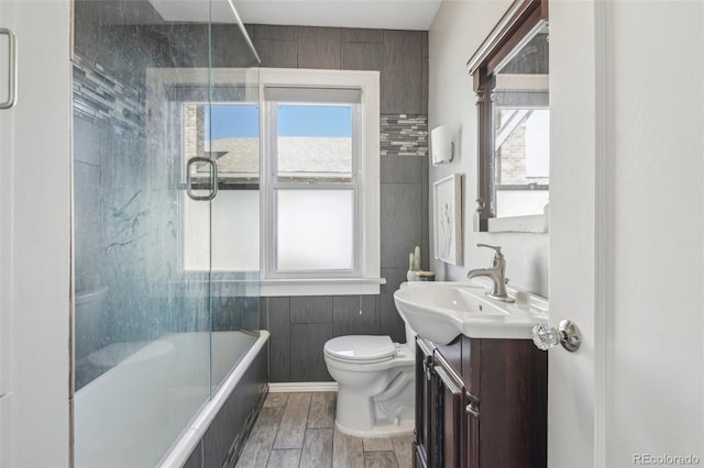 bathroom featuring vanity, toilet, shower / bath combination with glass door, and wood finish floors