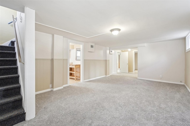 empty room featuring light carpet, wainscoting, and stairs