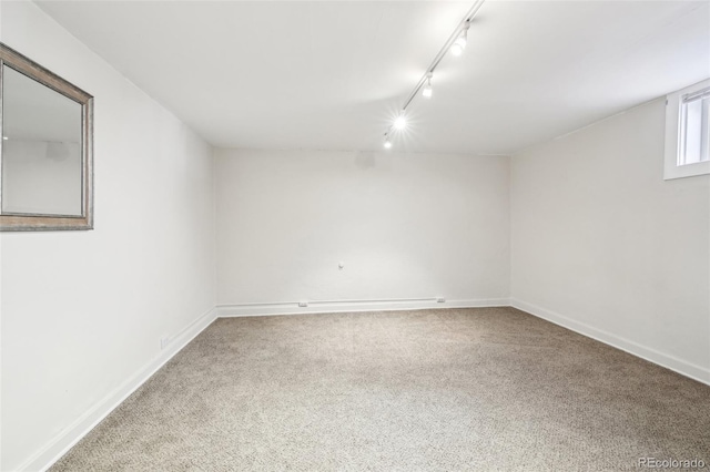 carpeted empty room with baseboards and rail lighting