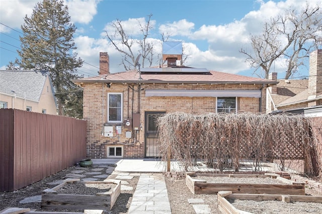 back of house with brick siding, a vegetable garden, and a chimney