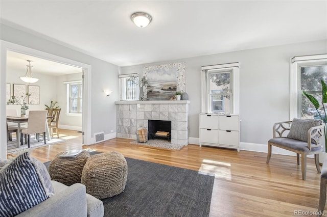 living room featuring a tile fireplace, wood finished floors, visible vents, and baseboards