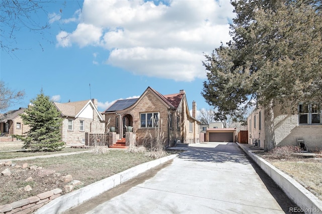 view of front of house with driveway, an outdoor structure, a garage, solar panels, and brick siding