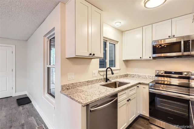 kitchen with white cabinets, dark wood-style flooring, light stone countertops, appliances with stainless steel finishes, and a sink