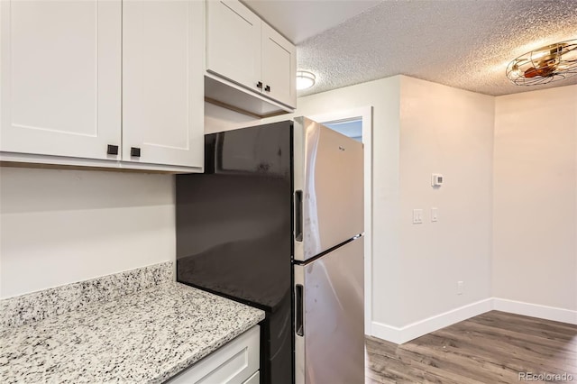kitchen featuring a textured ceiling, white cabinets, freestanding refrigerator, and wood finished floors
