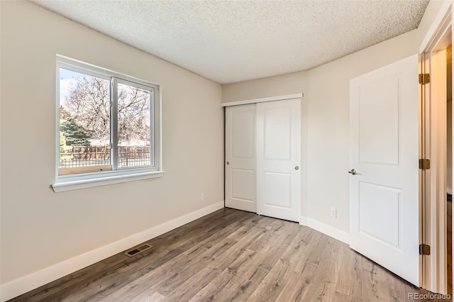 unfurnished bedroom featuring visible vents, a closet, baseboards, light wood-type flooring, and a textured ceiling