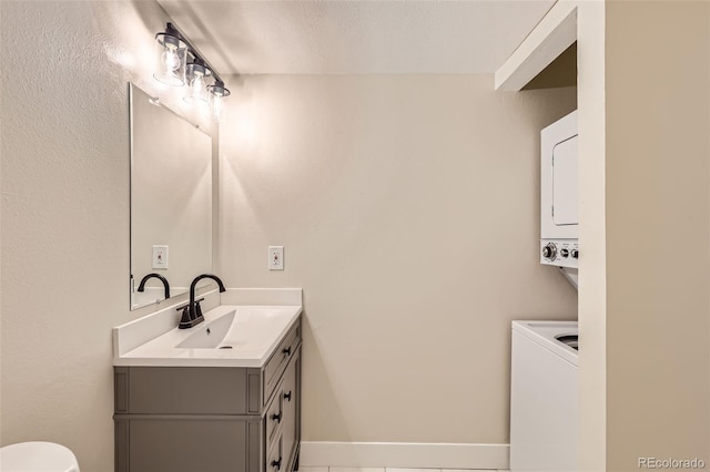 bathroom with toilet, stacked washer / drying machine, baseboards, and vanity
