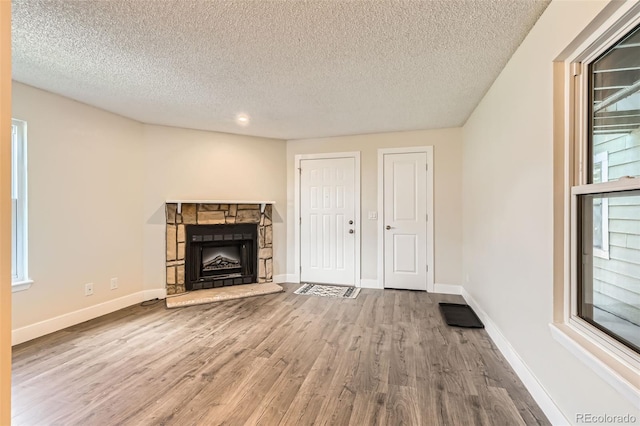 unfurnished living room with a textured ceiling, baseboards, a fireplace, and wood finished floors