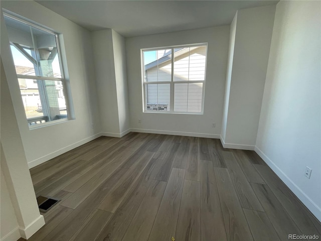 unfurnished room featuring dark wood-style flooring, visible vents, and baseboards