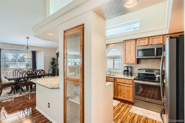 20336 E 48th Dr, Denver, CO 80249 - kitchen featuring appliances with stainless steel finishes, a sink, light wood finished floors, backsplash, and decorative light fixtures