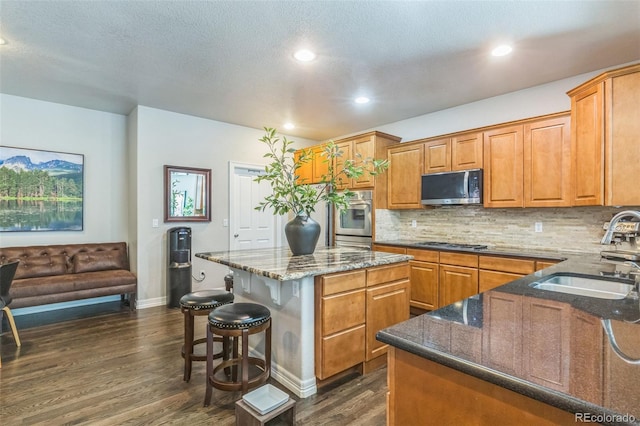 kitchen with dark wood-style flooring, a sink, dark stone countertops, backsplash, and stainless steel appliances