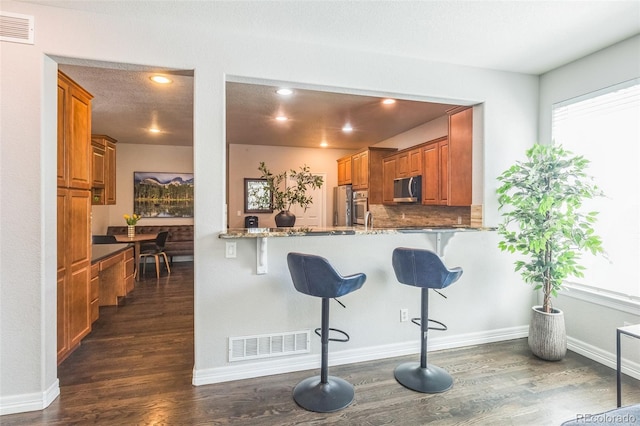 kitchen with stainless steel microwave, dark wood-style flooring, brown cabinetry, and visible vents