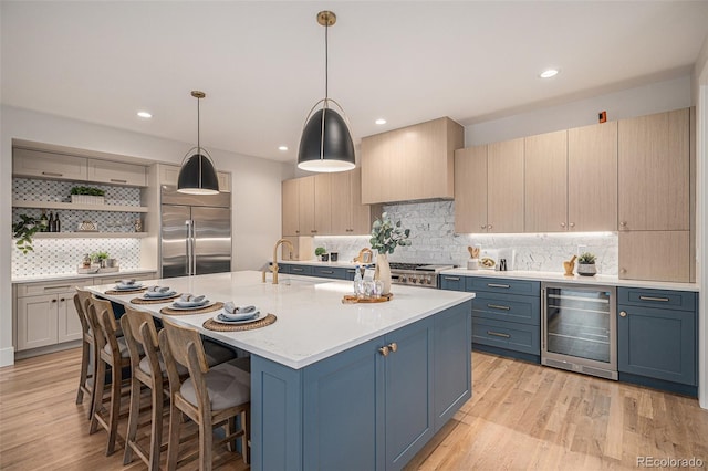 kitchen featuring beverage cooler, high end refrigerator, blue cabinets, pendant lighting, and a center island with sink