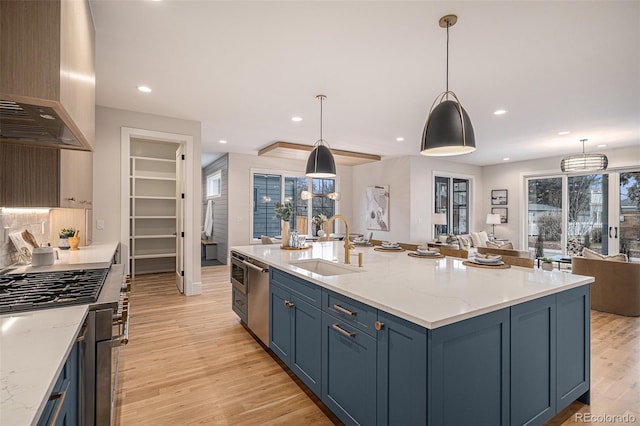 kitchen with blue cabinetry, sink, wall chimney exhaust hood, light stone counters, and pendant lighting