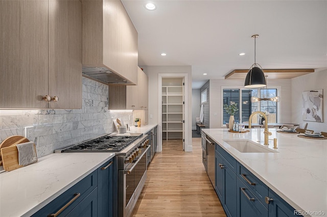 kitchen with hanging light fixtures, sink, blue cabinetry, appliances with stainless steel finishes, and light stone counters