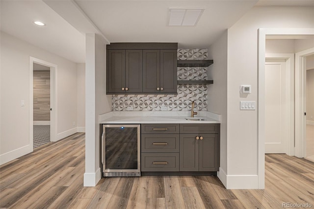 bar featuring decorative backsplash, light hardwood / wood-style floors, sink, and beverage cooler