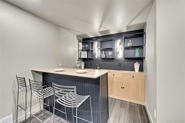 kitchen featuring dark hardwood / wood-style floors, light brown cabinetry, butcher block countertops, a kitchen bar, and kitchen peninsula