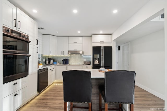 kitchen with a breakfast bar, tasteful backsplash, black appliances, white cabinets, and a kitchen island