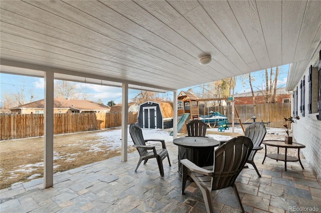 snow covered patio with a playground, a trampoline, and a shed